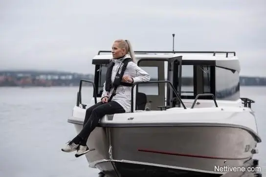 A woman in sportswear sits on the edge of a boat, overlooking calm water, with a cloudy sky in the background.